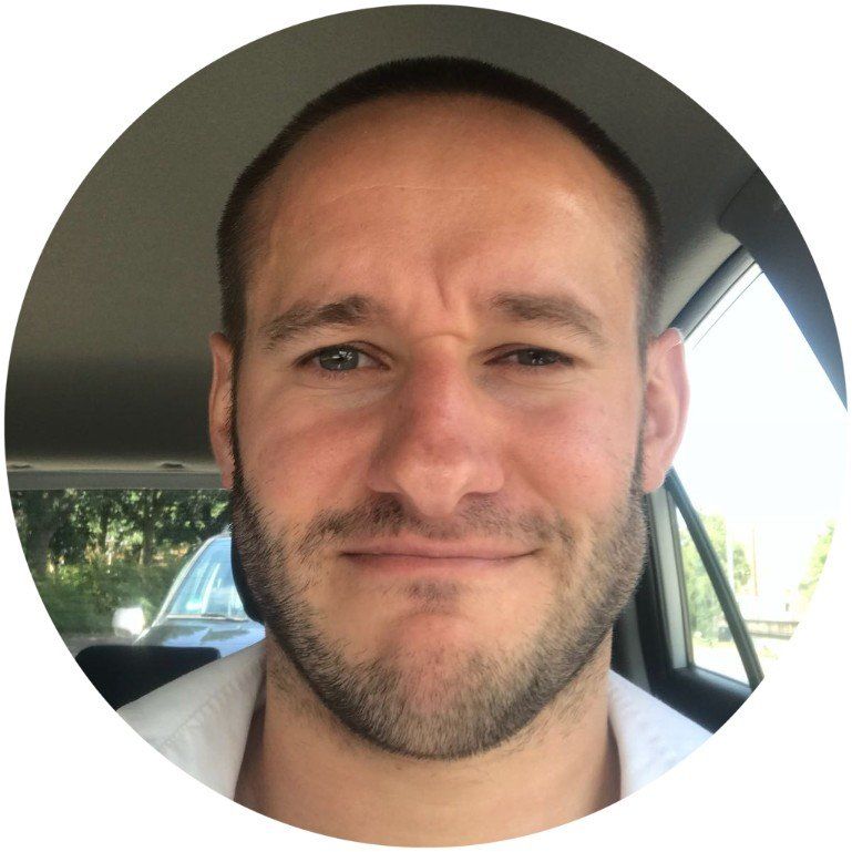 Een man met een baard lacht in een auto