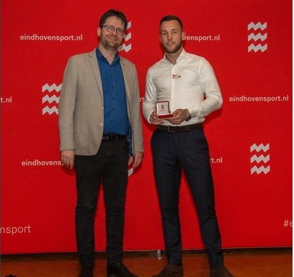 Twee mannen staan voor een rode muur met het woord sport erop