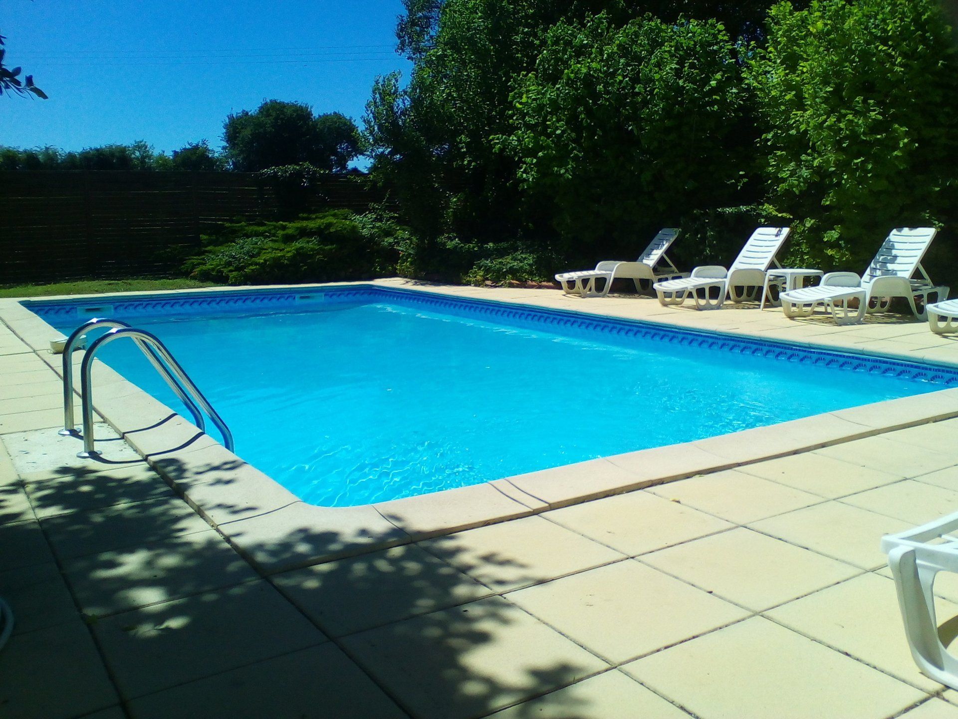 Blue swimming pool surrounded by cream terrace slabs