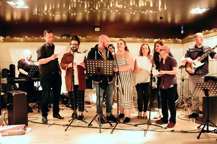 A group of people on stage in front of microphones, singing and playing musical instruments