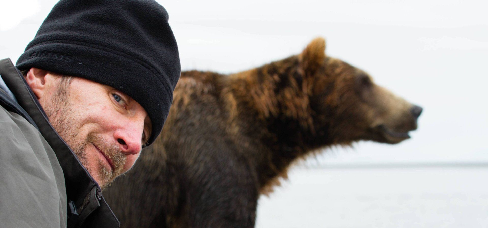 man smiling with a grizzly bear in the background