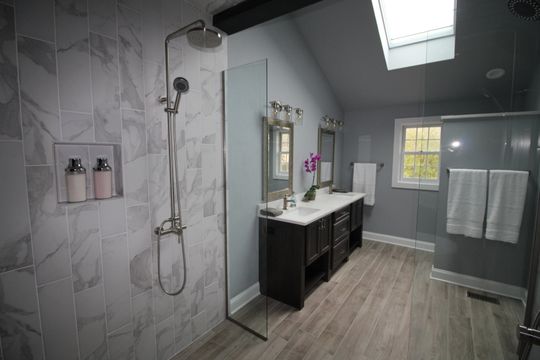 A bathroom with two sinks , a walk in shower and a skylight.