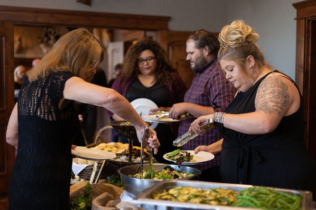 People serving themselves food from a buffet table at a gathering.