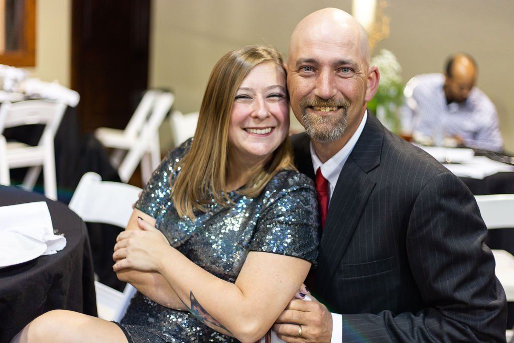 A smiling woman in a sequined dress and a smiling man in a suit posing together at an event.