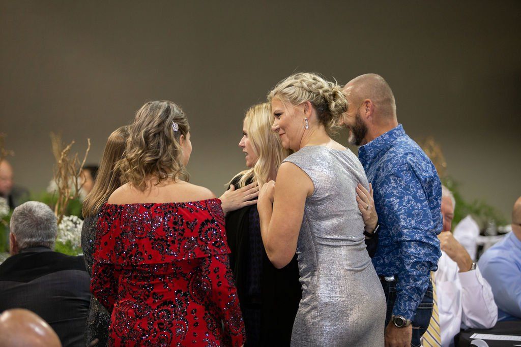 A group of people in formal attire socialize at an event, including individuals in sequined red and silver dresses.