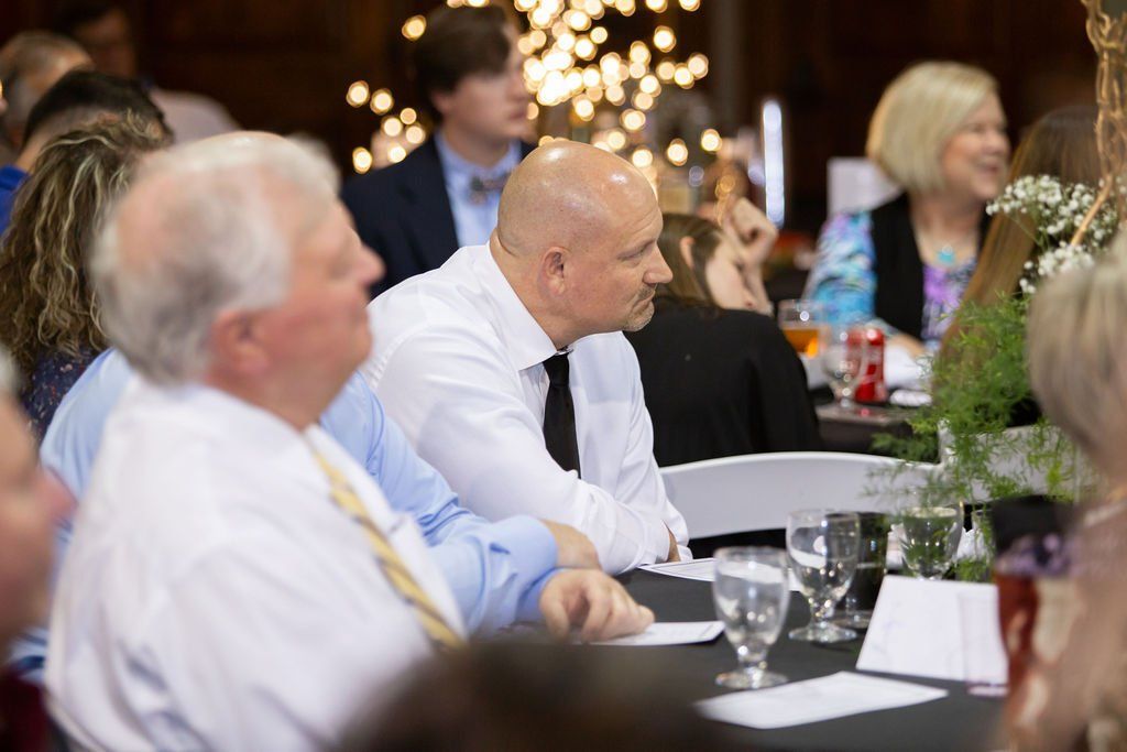 People seated at tables in a dimly lit banquet hall with twinkling lights in the background.