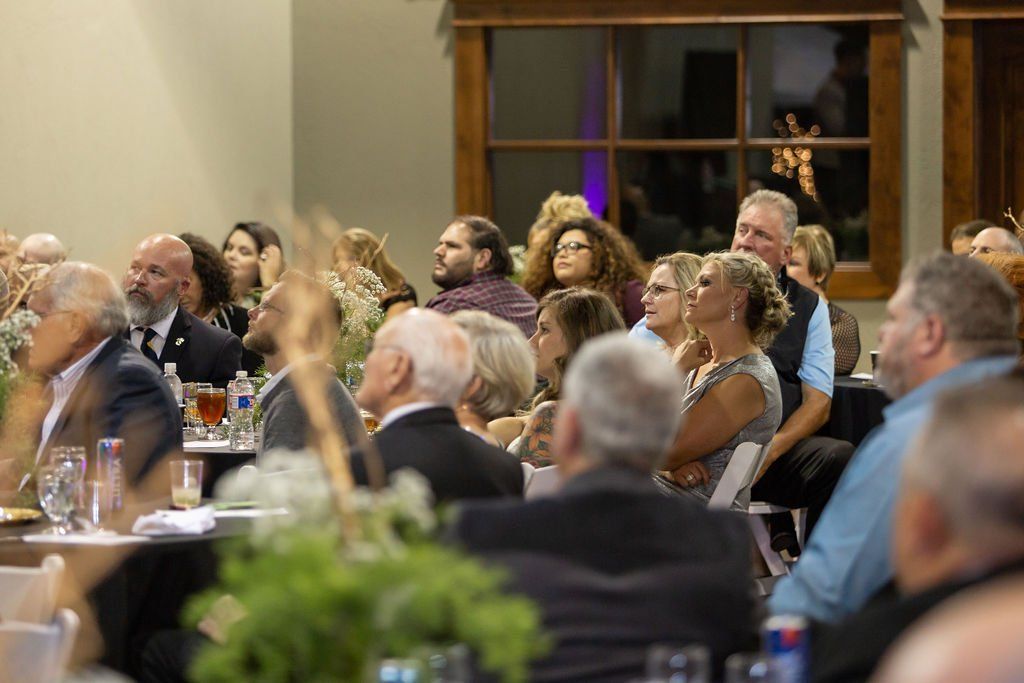 Attendees sit at tables in a dimly lit, wood-accented room, listening intently to a presentation.