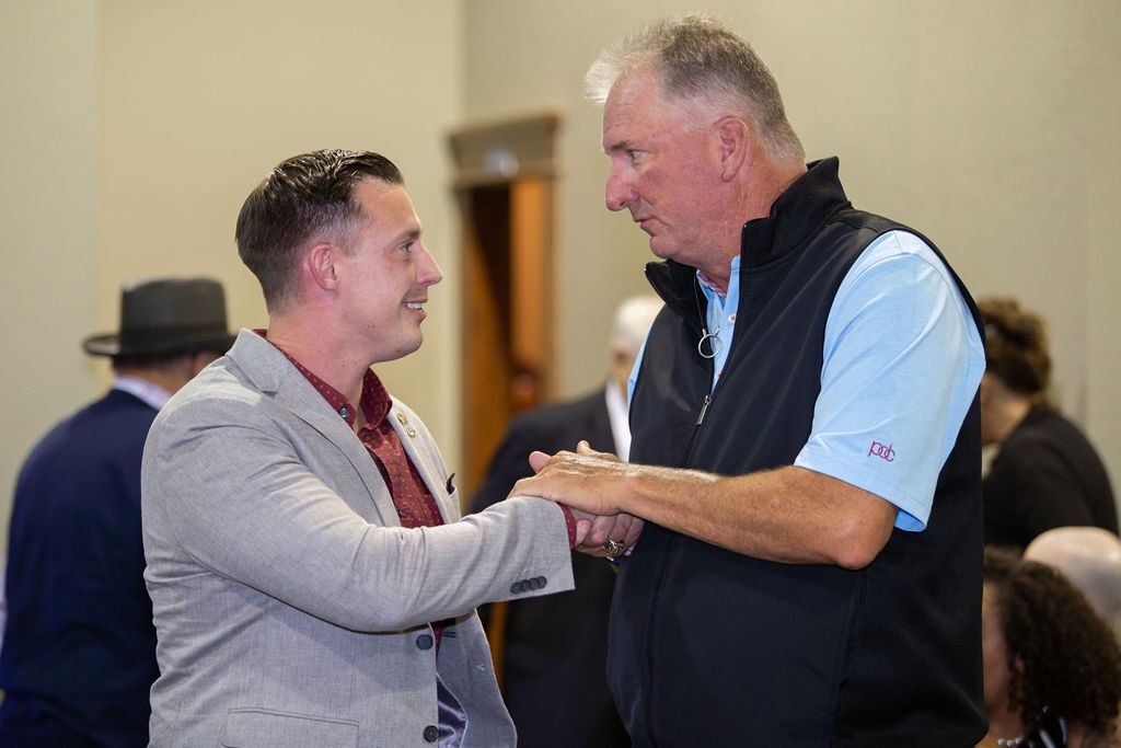 Two men in business casual attire shaking hands while facing each other in an indoor setting.