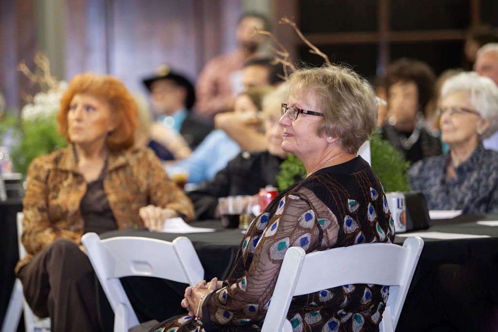 People sitting at tables in a room, focusing on a presentation or event.