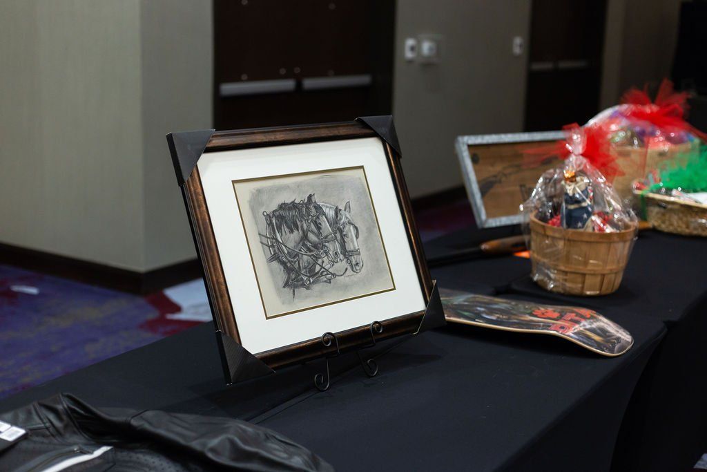 A framed black-and-white abstract sketch sits on a black table next to gift baskets and a skateboard.