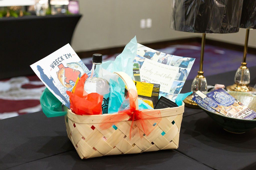 A woven gift basket filled with colorful paper, a small bottle, and a card, resting on a black table.