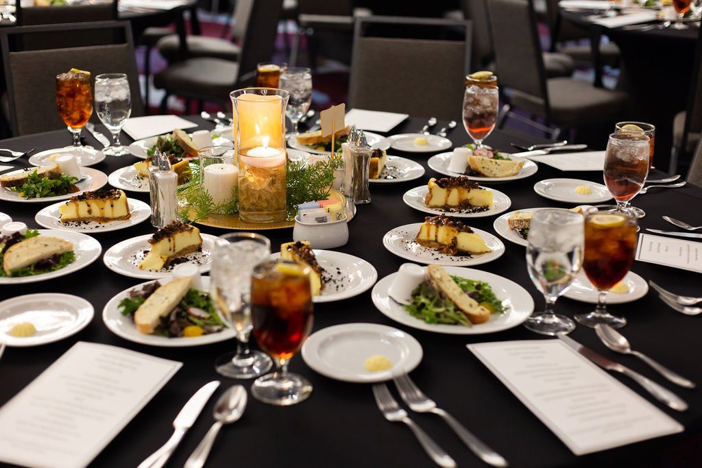 A dining table set for an event with multiple plates of salad, dessert, glassware, and a central candle centerpiece.