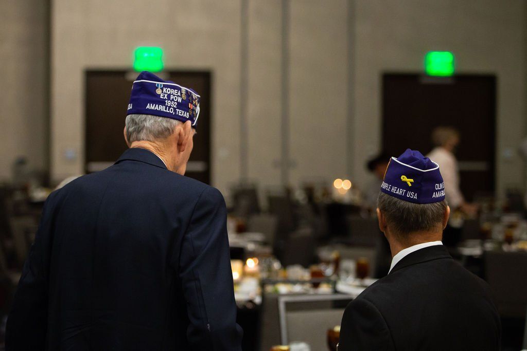 Two people in suits and blue American Legion-style garrison caps stand in a banquet hall.