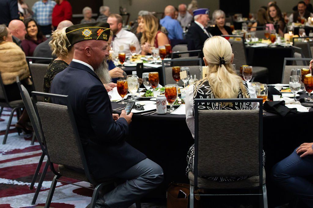 Attendees at a formal banquet dinner, with a person in a veteran cap in the foreground.