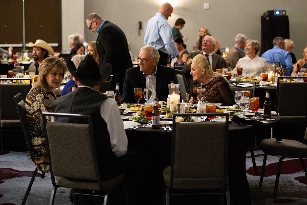 People seated at round tables in a banquet hall, enjoying a formal dinner event with drinks and conversation.