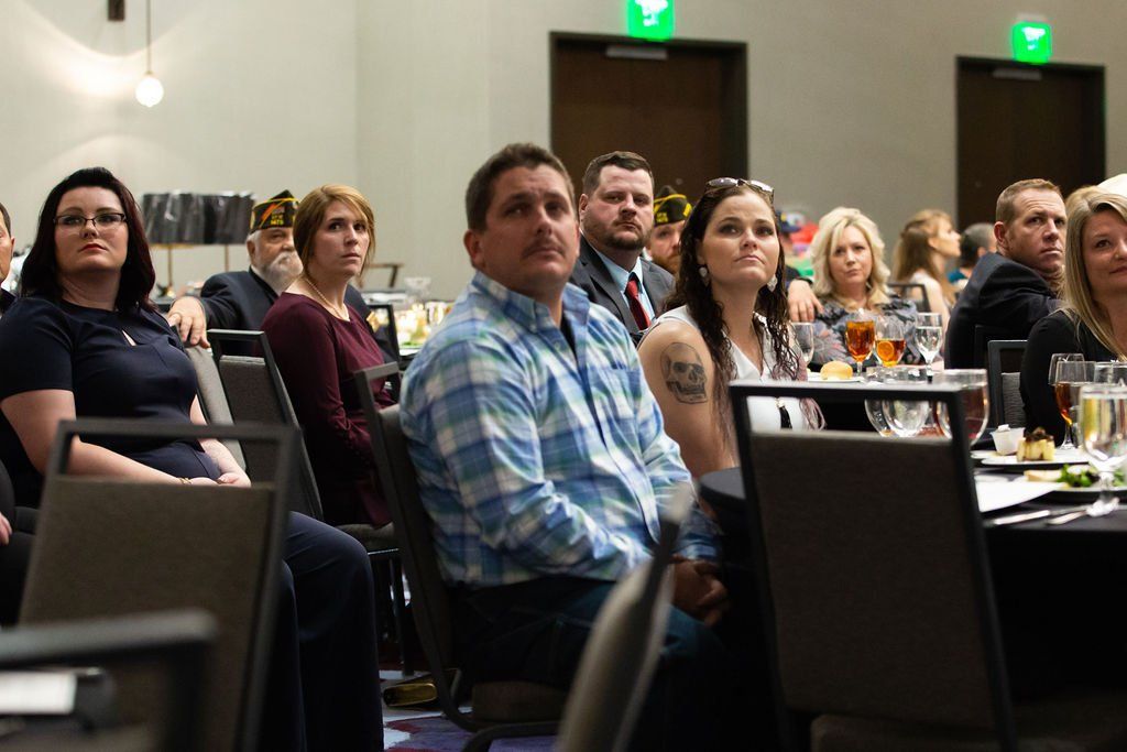 A group of people sitting at tables in a conference room, listening intently to a presentation.