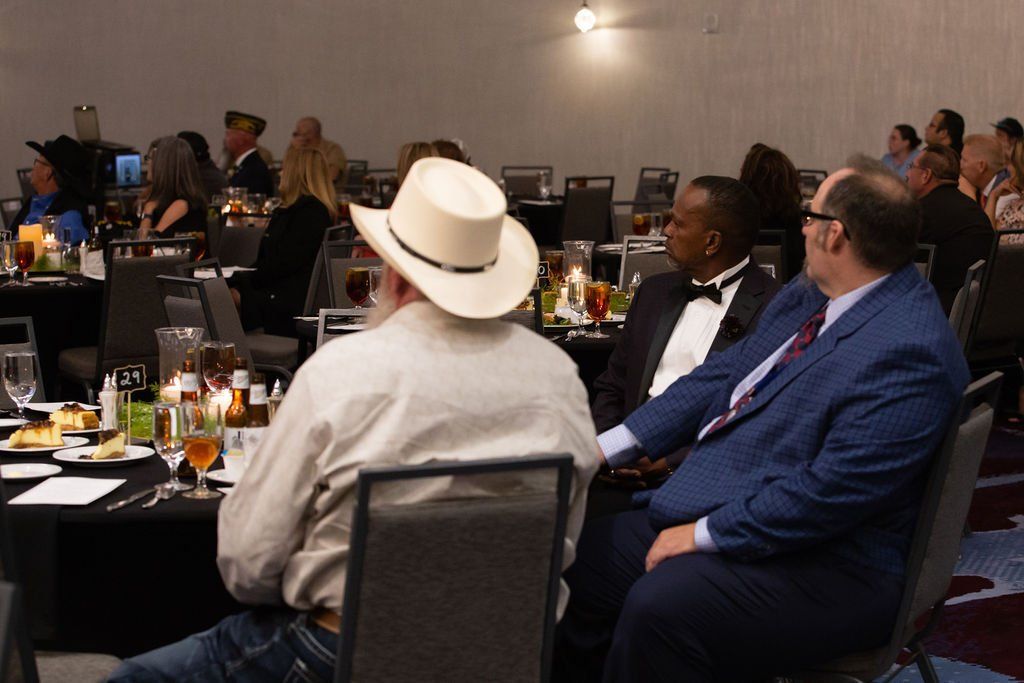 Attendees at a formal event sit at round tables, facing toward the front of the room.