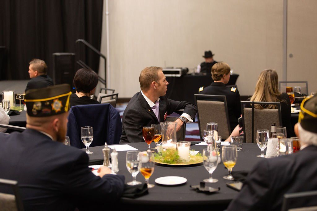 People in formal and military attire seated at round dining tables in a conference hall.