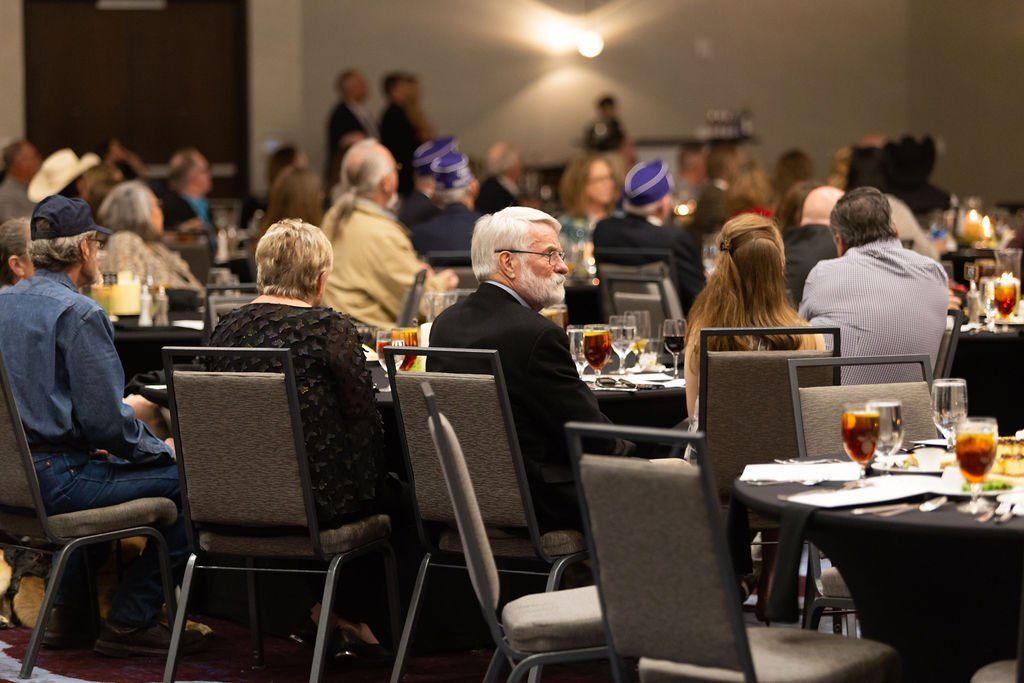 A group of people sits at round tables in a conference hall during an event.