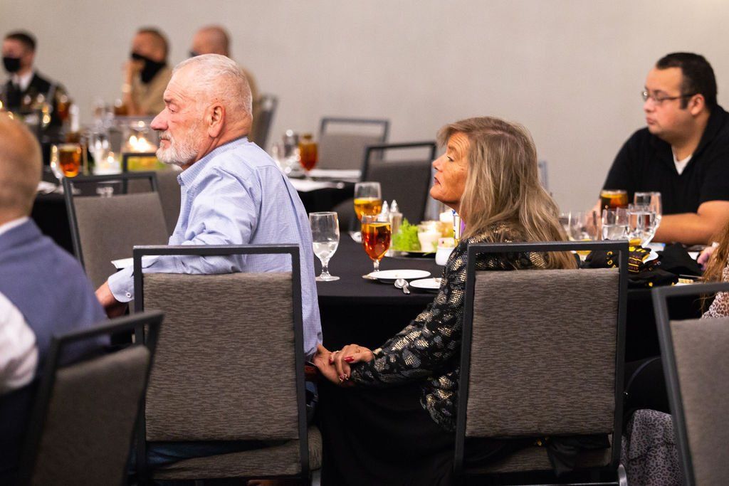 A couple sits at a table in a banquet hall, holding hands while looking away from the camera.