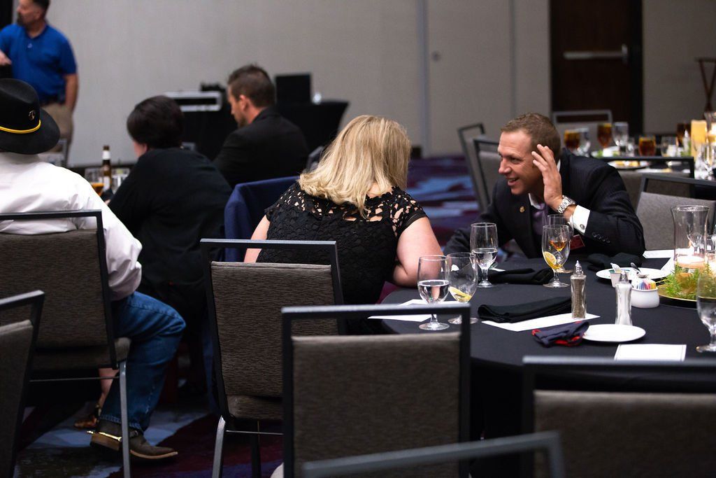 People seated around tables at a formal event, with a man and woman engaged in conversation.