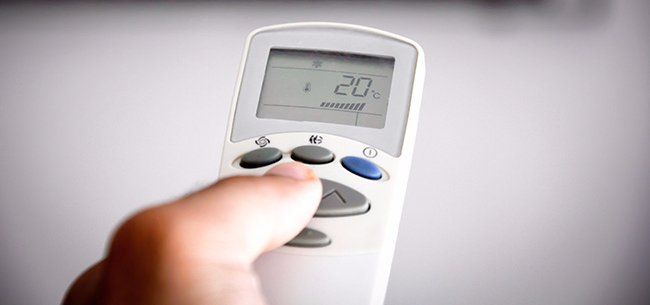 Hand holding a white remote, pressing a button to adjust the temperature, with a display showing 