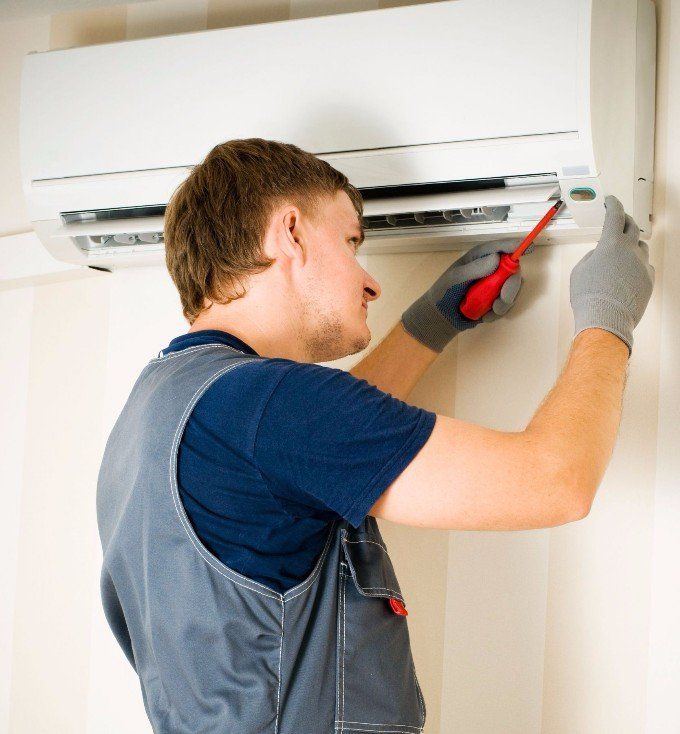 HVAC technician using a screwdriver to repair a wall-mounted air conditioner unit.