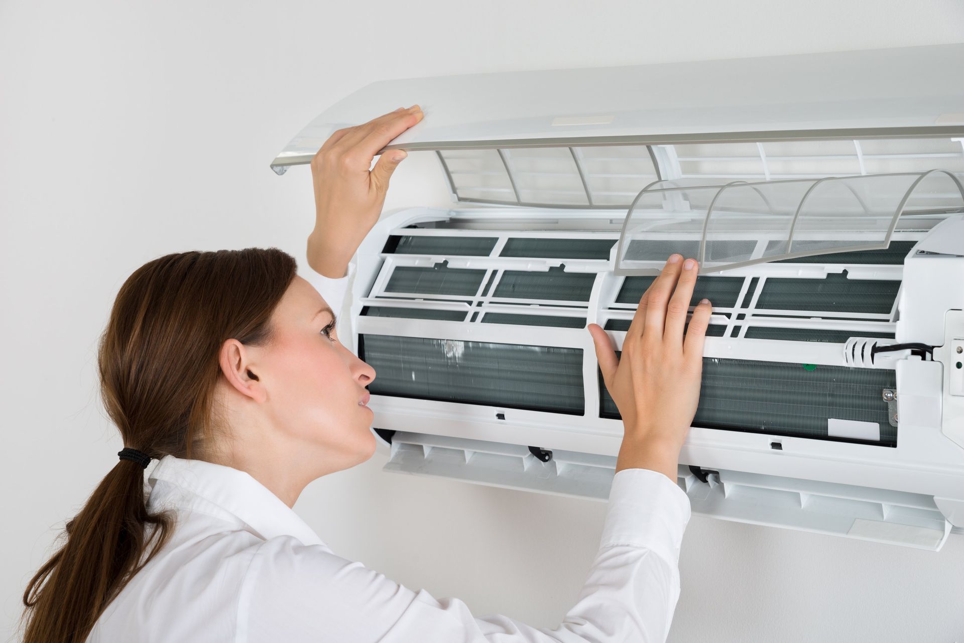 Woman cleaning an air conditioner filter. Hands near filter, white wall.