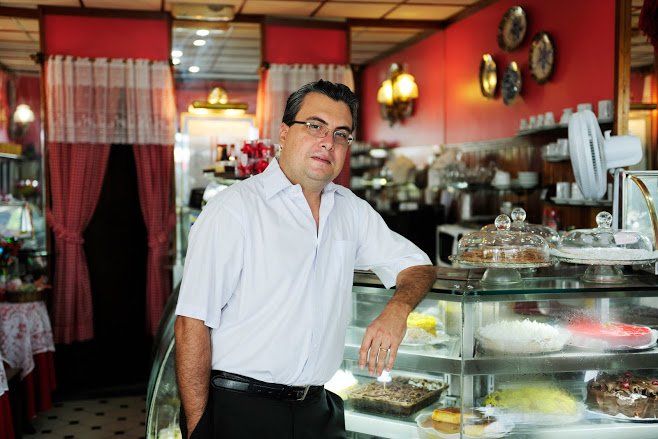 Man in white shirt leaning on a glass display case in a red-walled cafe.