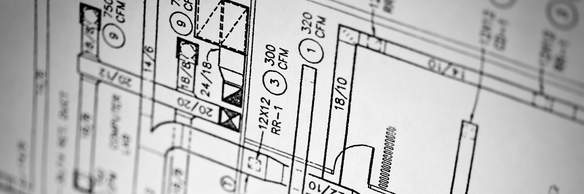 Close-up of a grayscale blueprint with technical drawings, lines, and symbols, likely for architectural or engineering design.