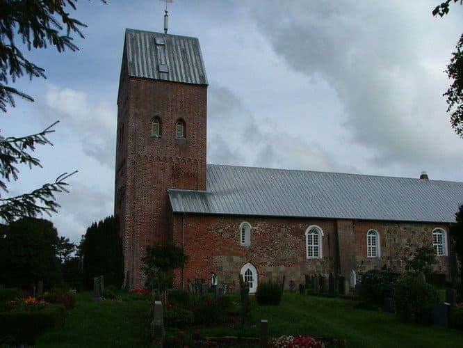 A brick church with a tall tower, green grass, and a cloudy sky.