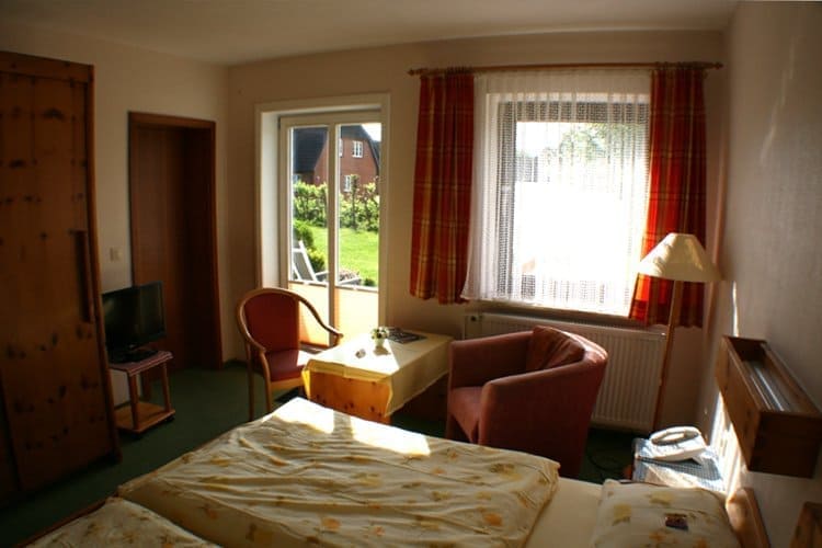 A hotel room with a bed, small table with chairs, and a door leading to an outdoor patio. Sun shines through the window.