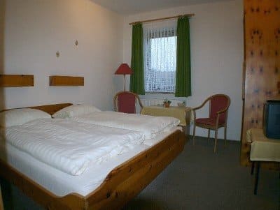 Bedroom with a wooden bed, two red chairs, and a small table by a window with green curtains.