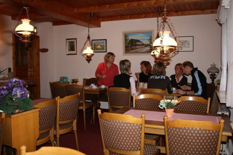 People gather around tables in a cozy, wood-paneled dining room, illuminated by vintage hanging lamps.  