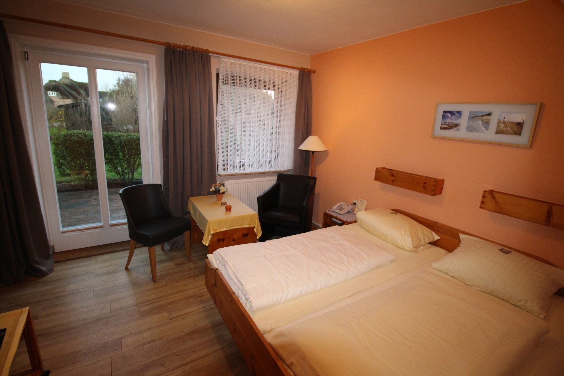 A hotel room with a bed, chairs, and a table by a window and sliding door. The walls are peach colored.