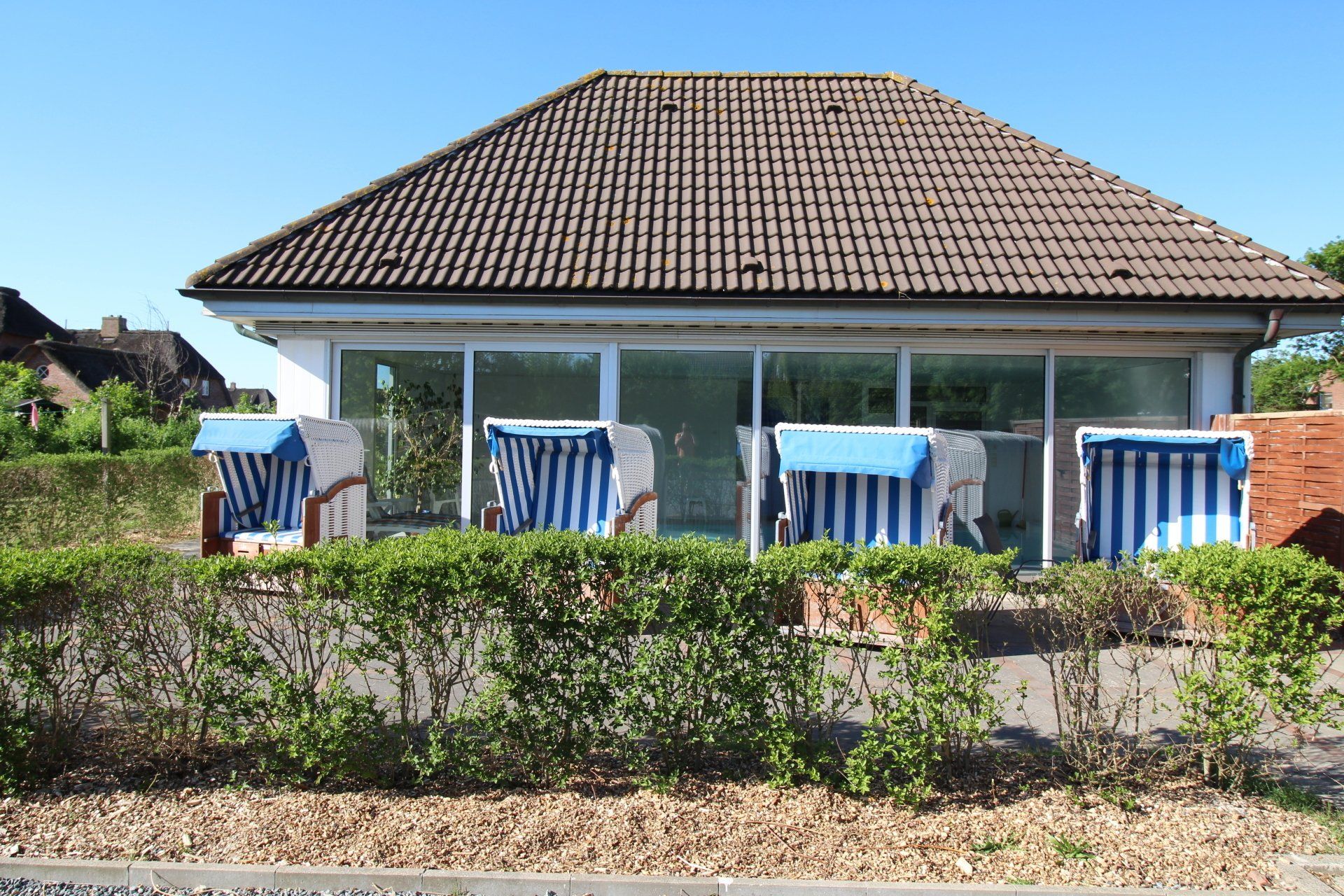 Beach chairs with blue and white stripes in front of a building with a brown tiled roof, under a bright blue sky.