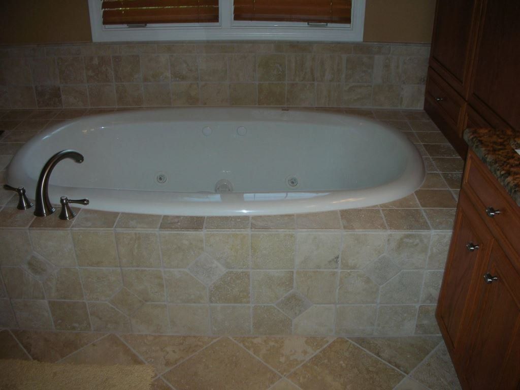 Bathtub set in tiled enclosure, dark fixtures, and wood cabinets.