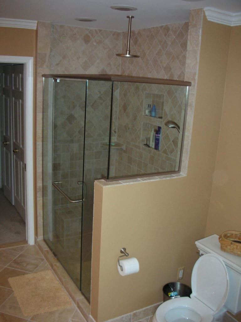 Bathroom with glass shower doors and tan tile. Toilet and neutral walls.