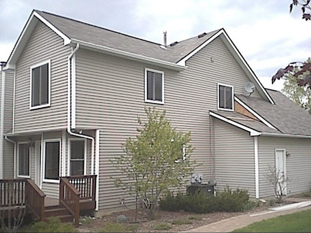 Two-story house with gray siding, white trim, dark roof. A small tree stands in front.