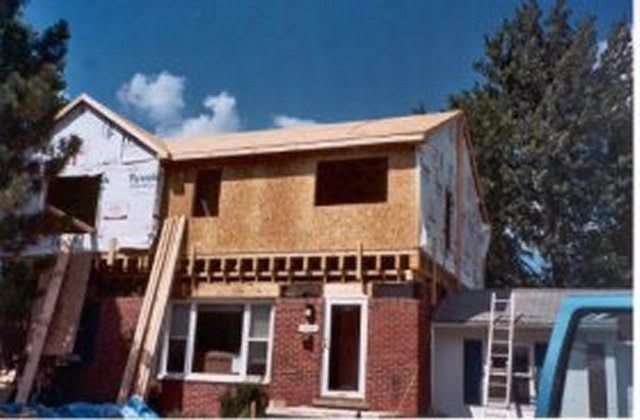 House under construction with exposed wood framing, brick facade, and blue sky.