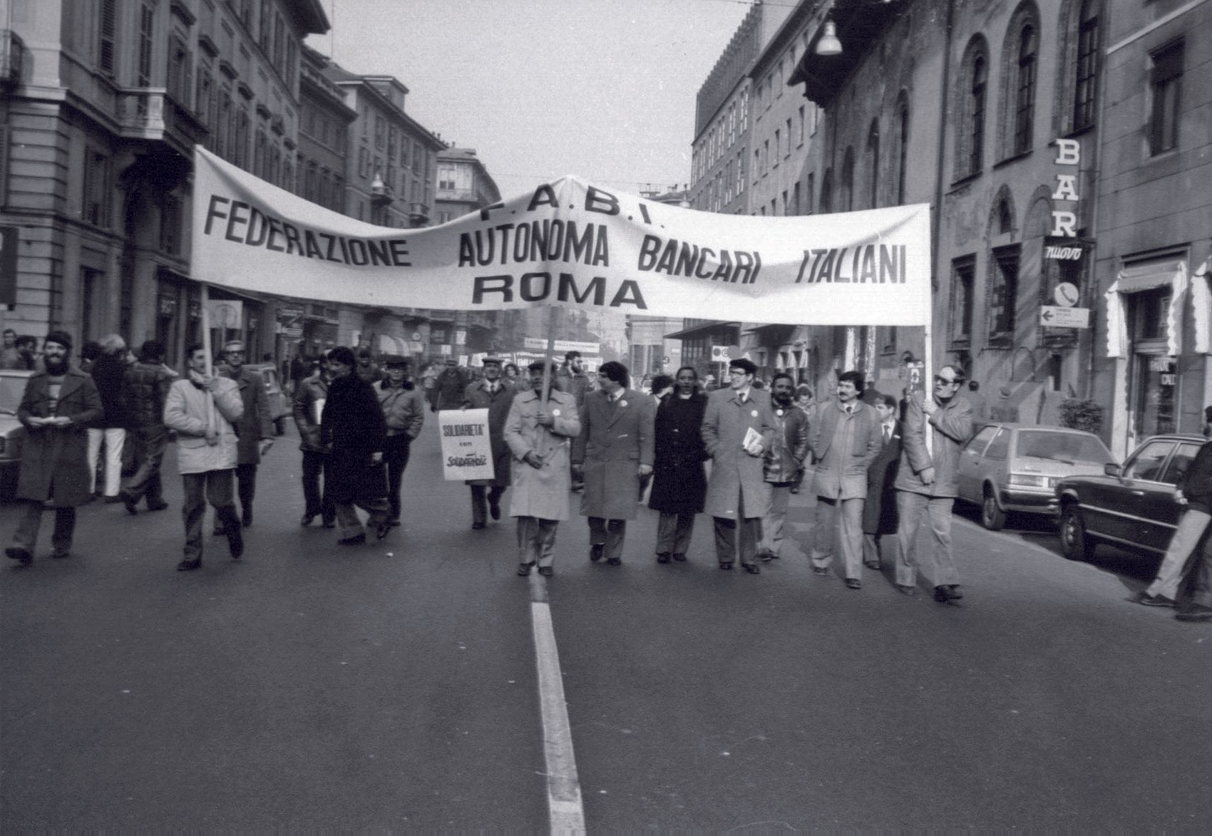Un gruppo di persone marcia per strada con uno striscione con la scritta ROM