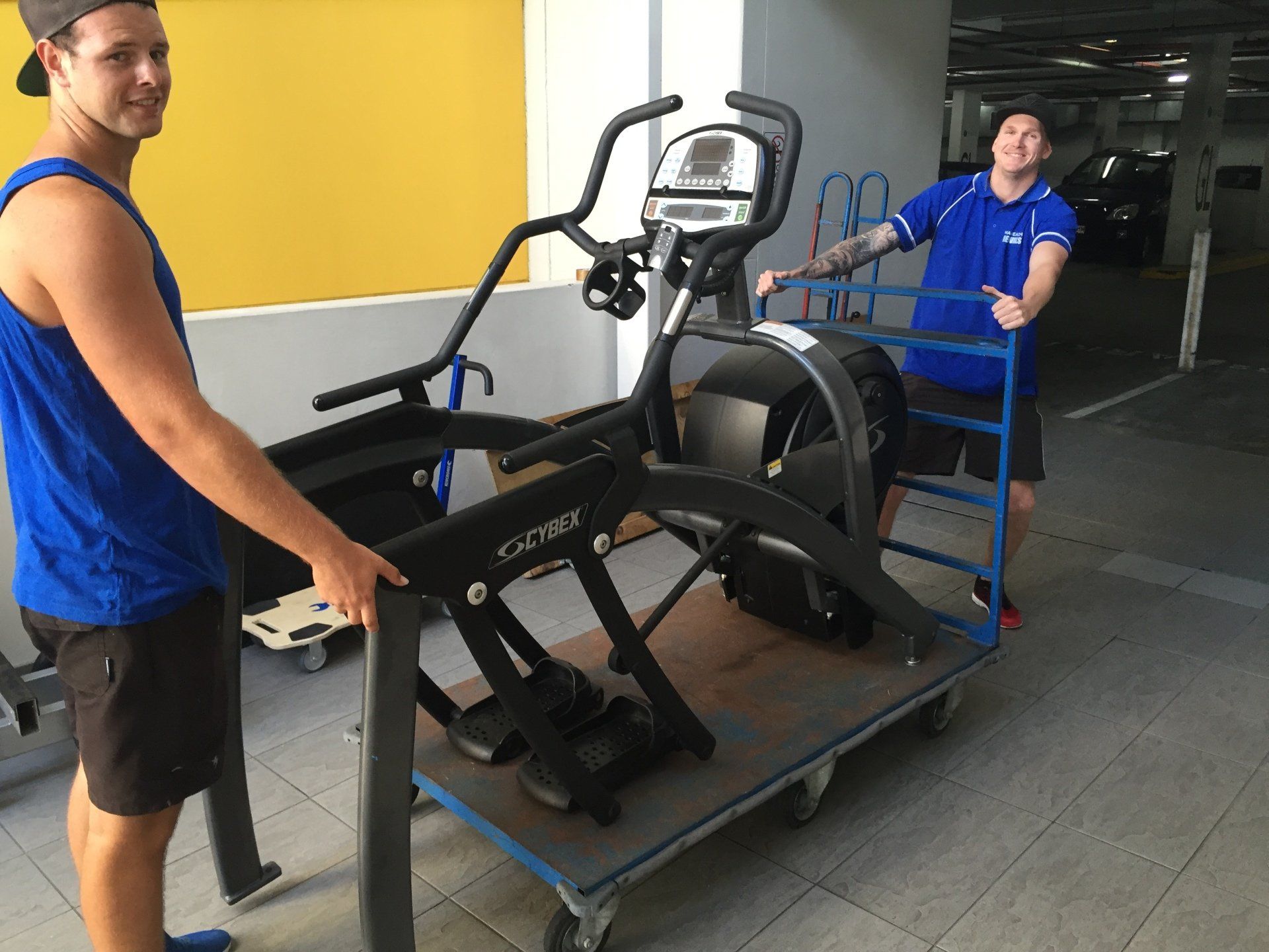 Two men are moving a treadmill on a cart.