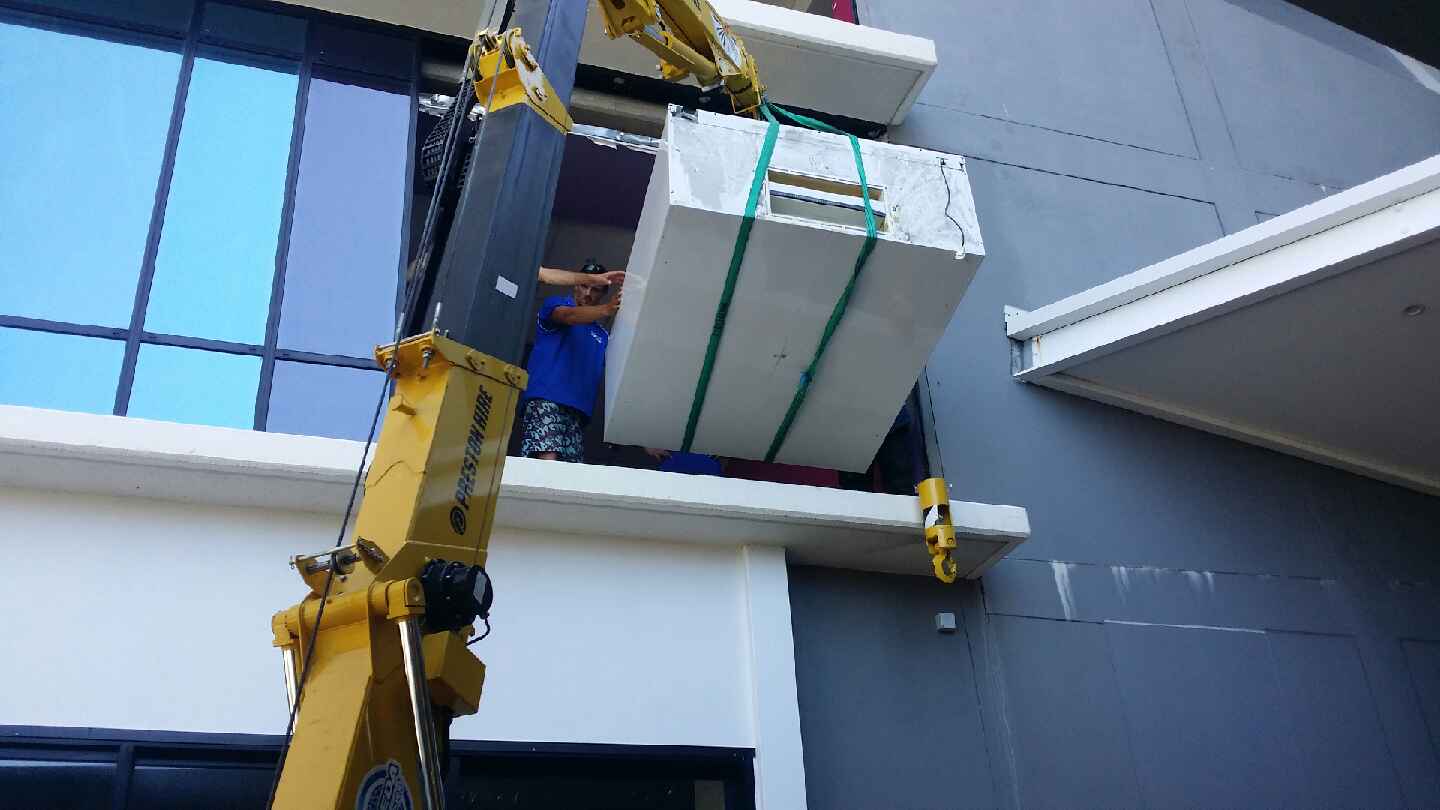 A yellow crane is lifting a large white box on top of a building.
