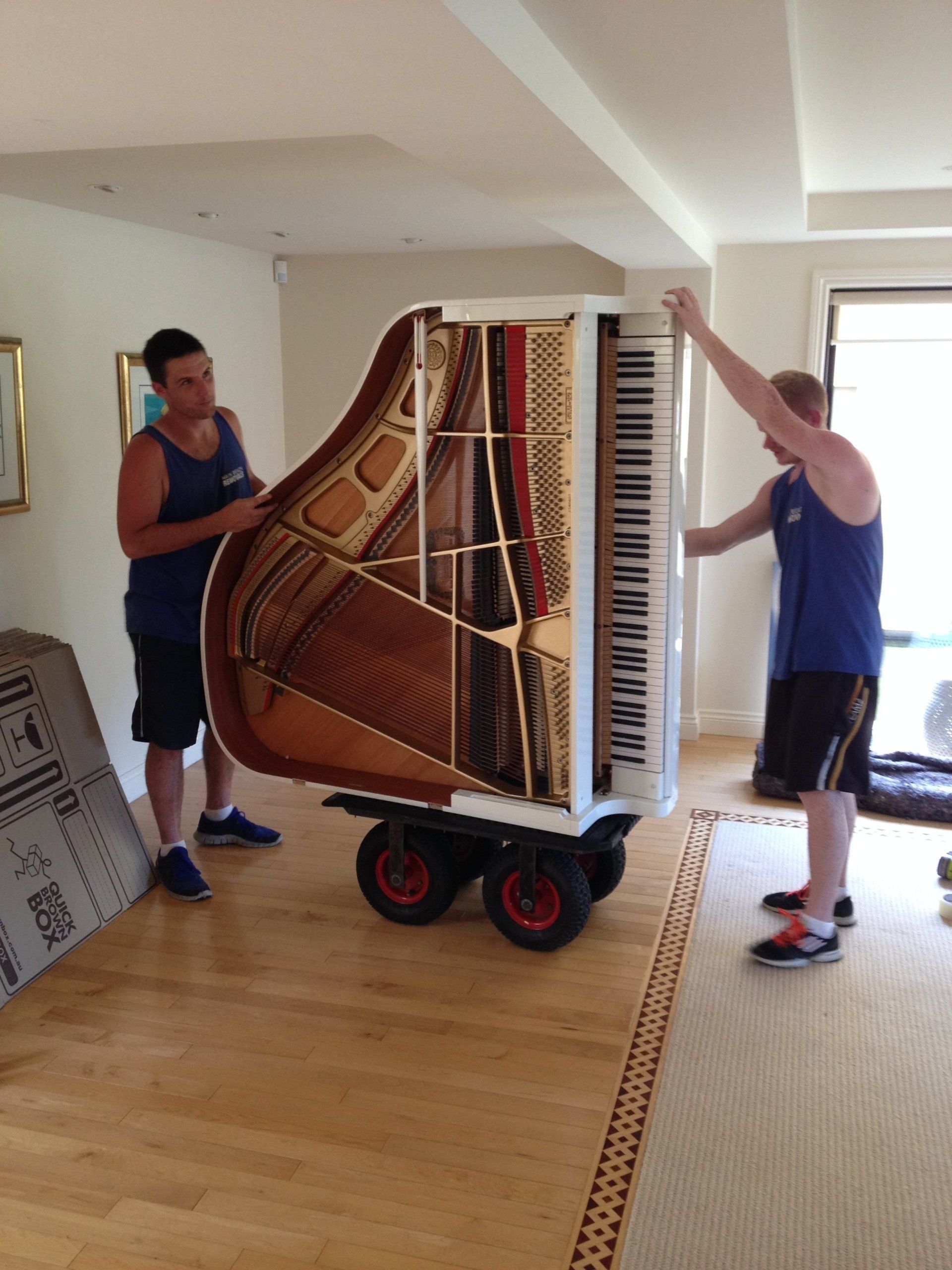 Two men are moving a piano on wheels in a living room