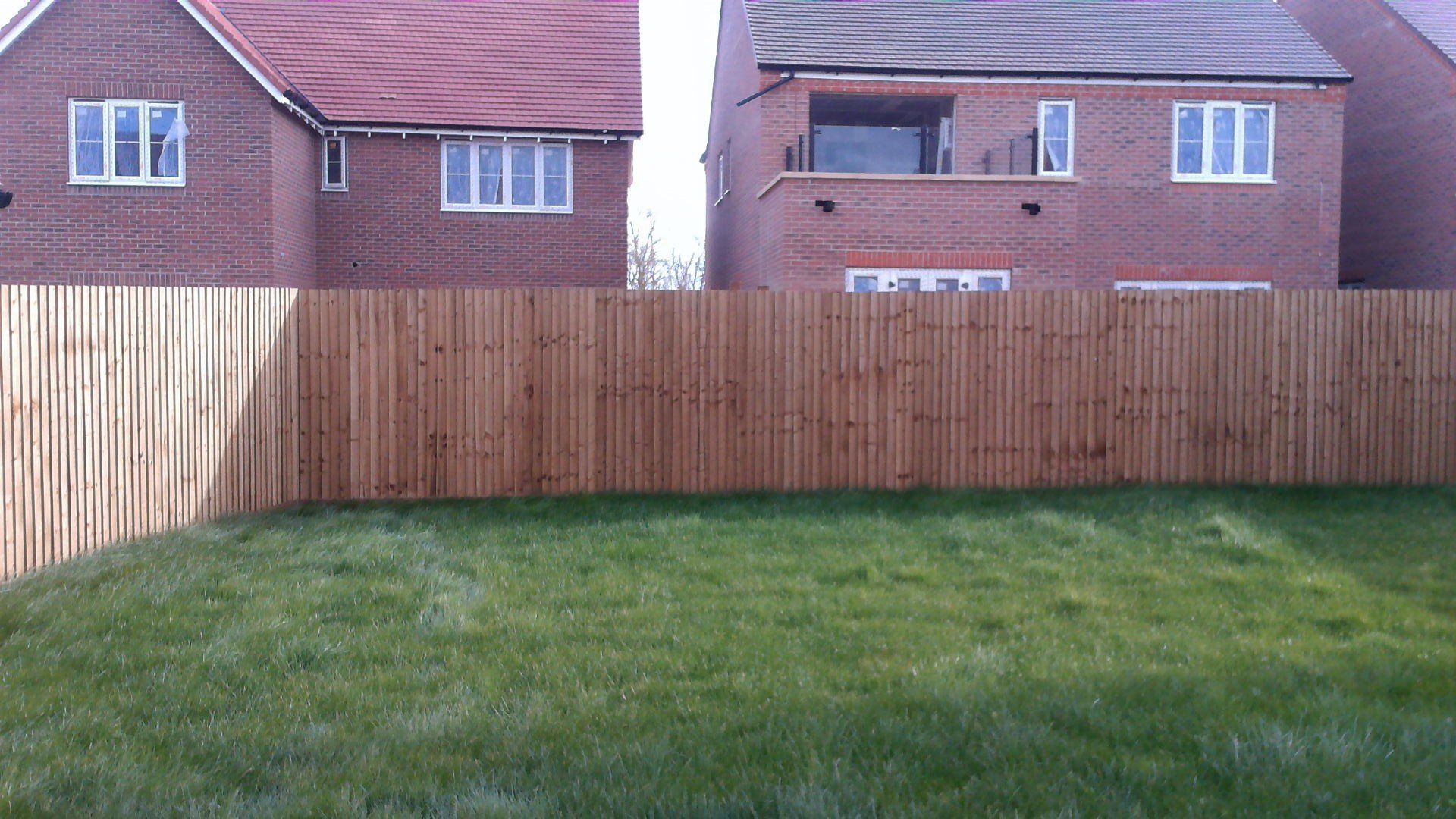 Wooden fence separating green lawn from two brick houses.