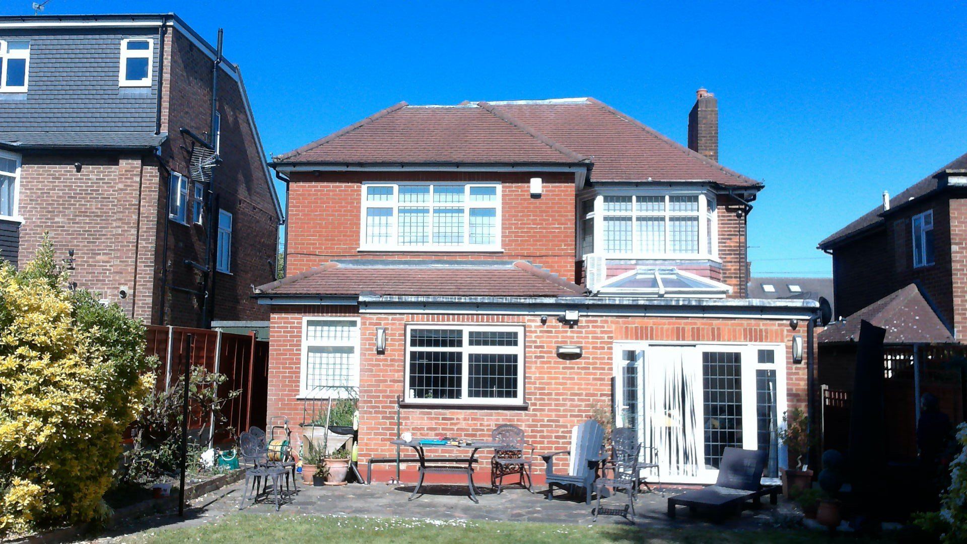 Red brick house with a tiled roof, french doors, and a small patio in a garden.