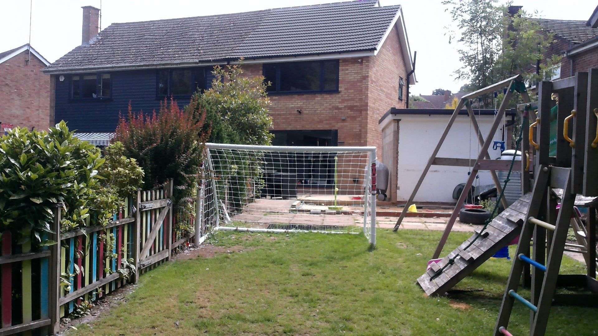 Backyard with a soccer goal, swing set, and a two-story brick house with a dark roof.