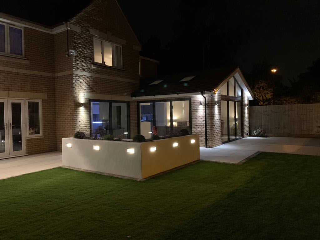 Night view of a modern house with outdoor lighting illuminating the exterior and yard.