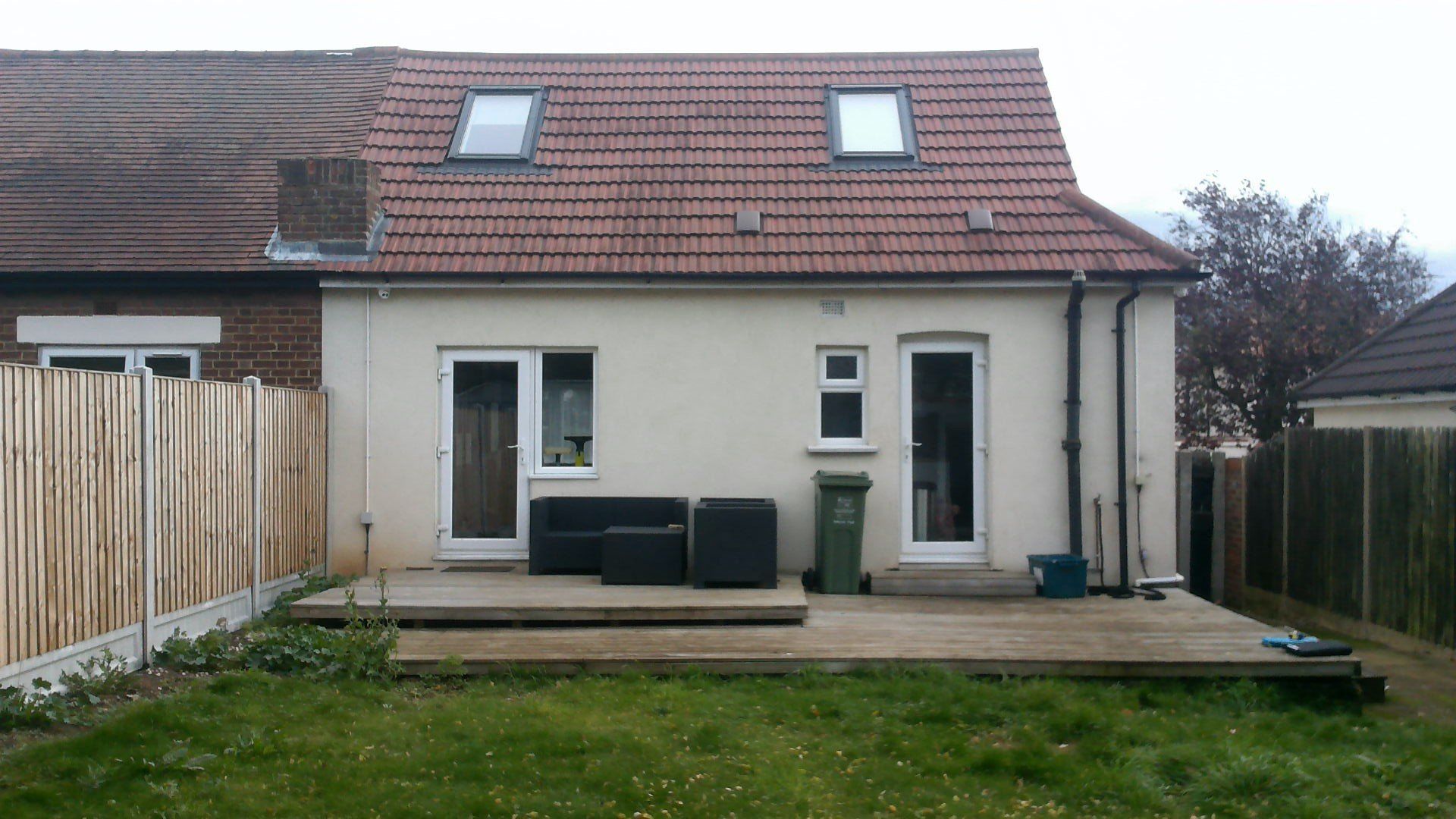 Backyard view of a house with a deck, garden, and wooden fence. The roof has two skylights.