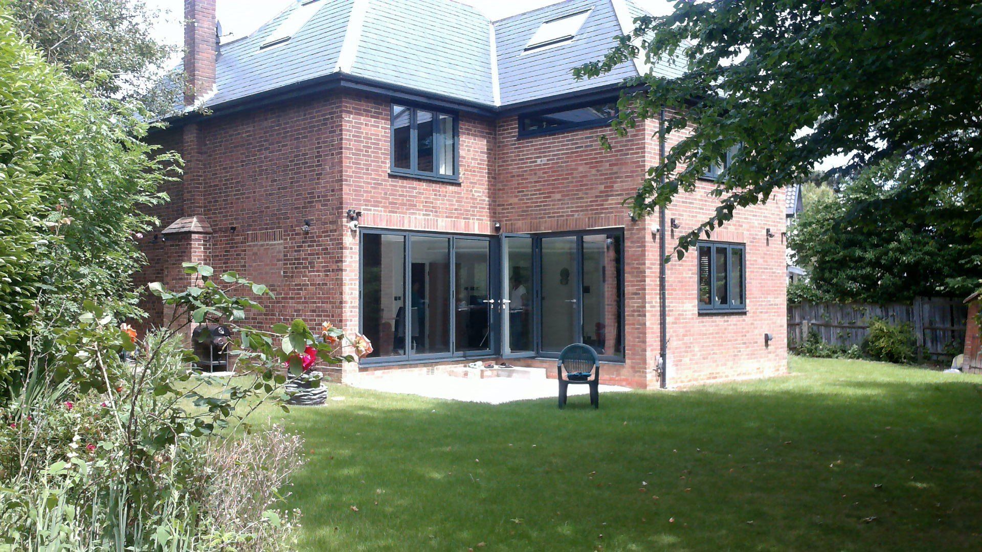 Brick house with large glass doors, surrounded by green lawn and garden.
